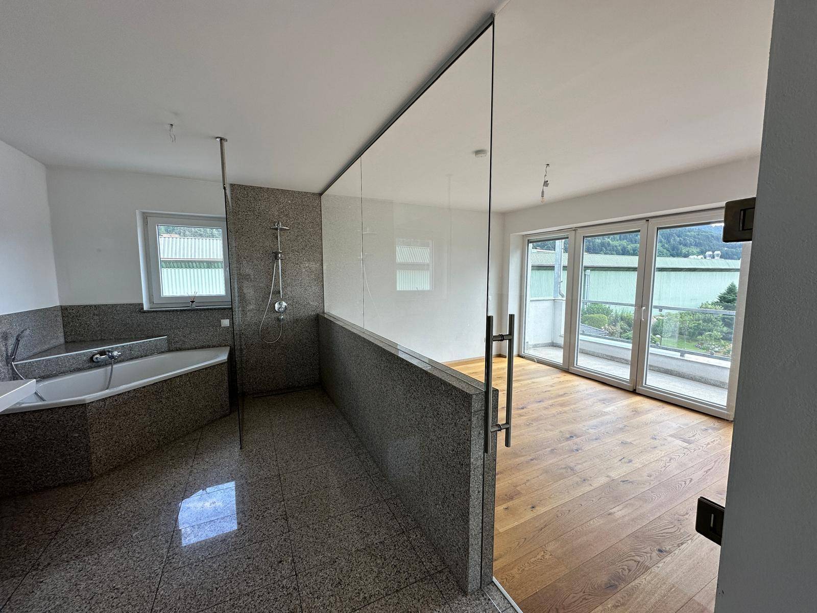 Modernes Badezimmer mit Eckbadewanne, Dusche und Glasabtrennung, angrenzend an ein Schlafzimmer.