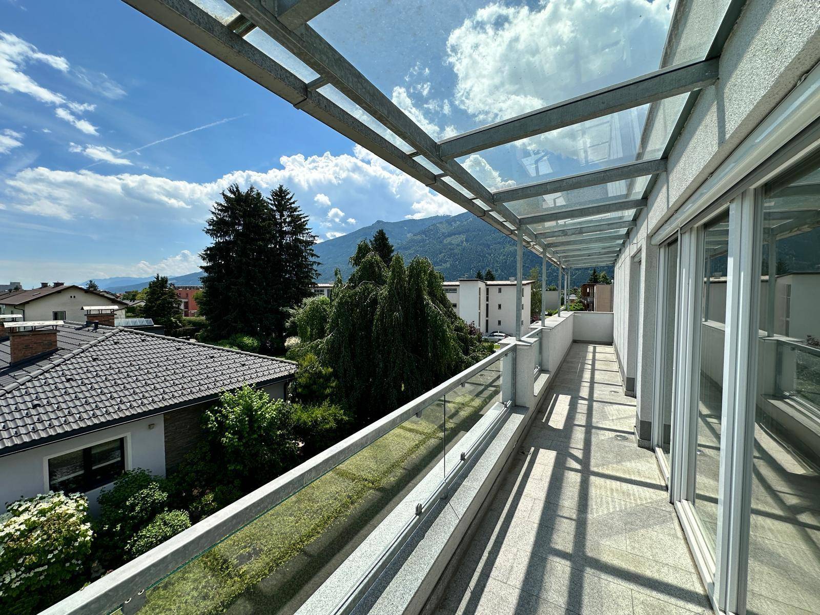 Lange, überdachte Terrasse mit Glasdach und Bergblick, ideal für entspannte Stunden im Freien.