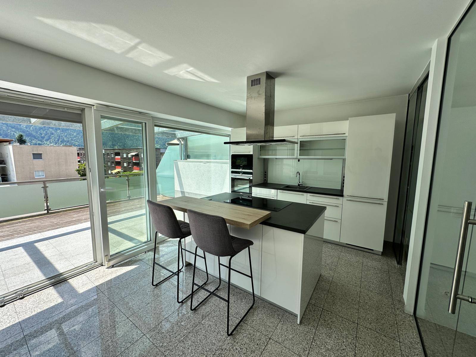 Moderne Einbauküche mit Kochinsel, weißen Hochglanzfronten und Zugang zur sonnigen Terrasse.
