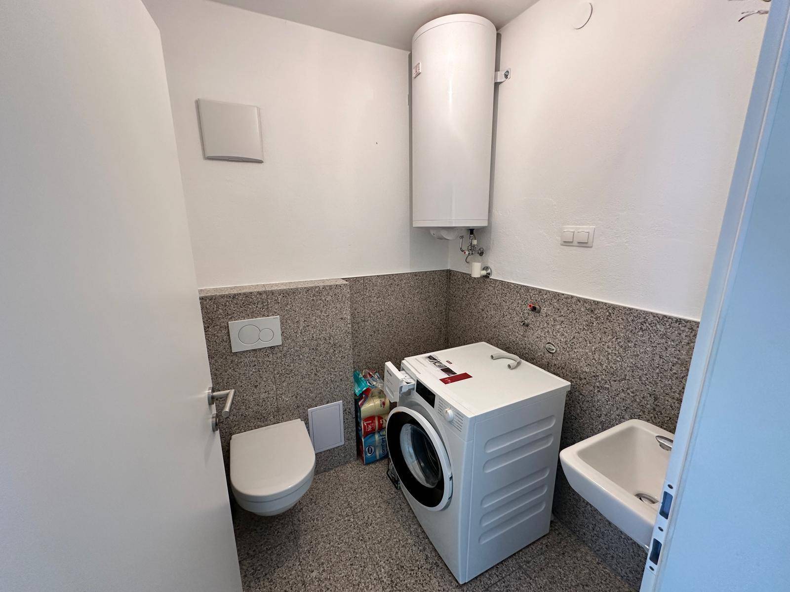 Kleiner Hauswirtschaftsraum mit WC, Waschmaschine und Warmwasserboiler auf Fliesenboden.