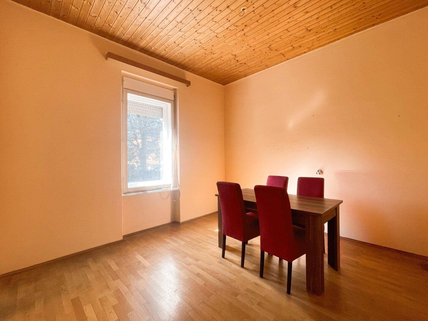 Esszimmer mit Holztisch, roten Stühlen und einer charakteristischen Holzpaneeldecke.