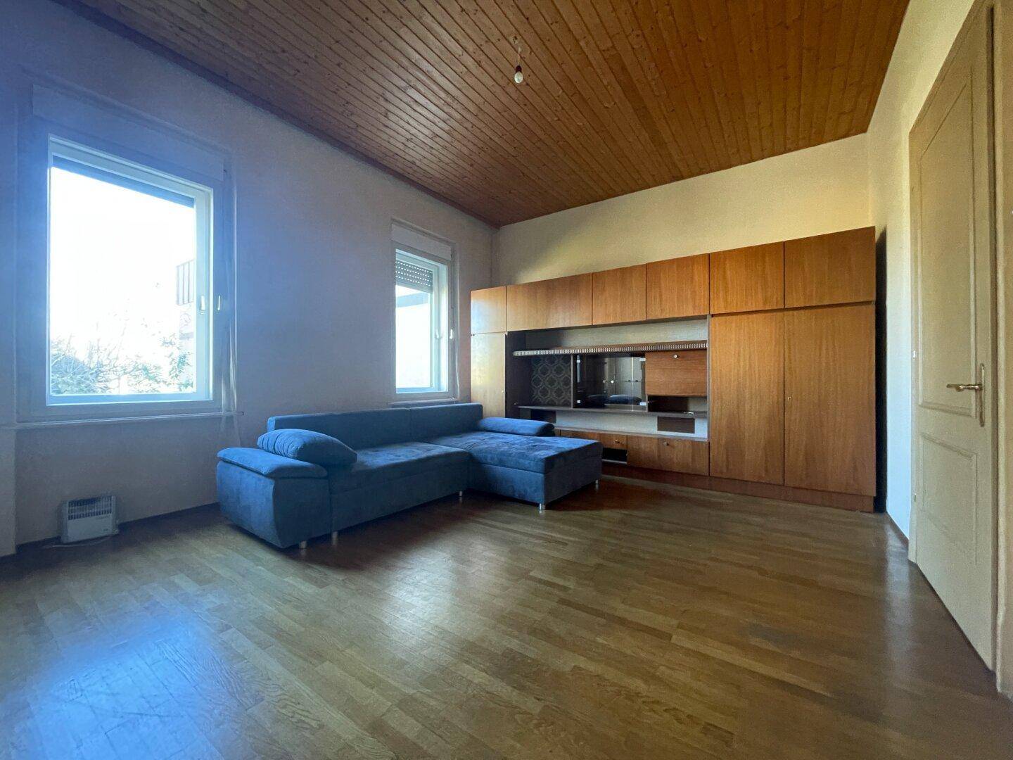 Gemütliches Wohnzimmer mit blauer Eckcouch, Holzdecke und integrierten Holzschränken.
