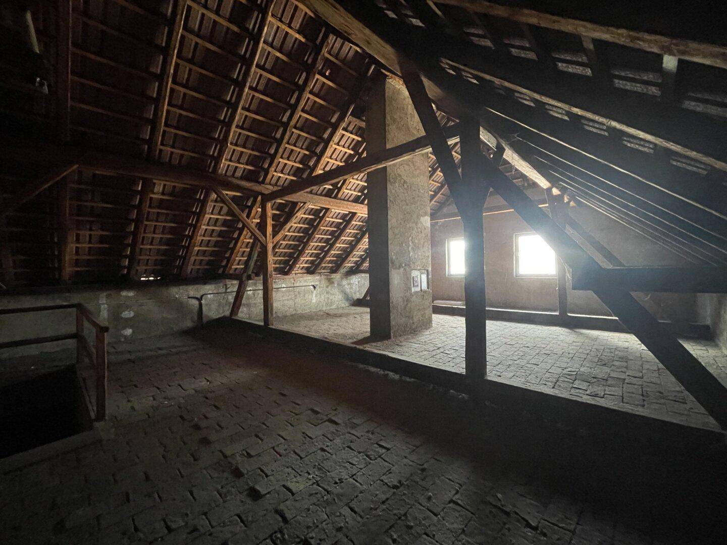 Geräumiger Dachboden mit sichtbaren Holzbalken und Ziegelboden, bereit für Ausbau.