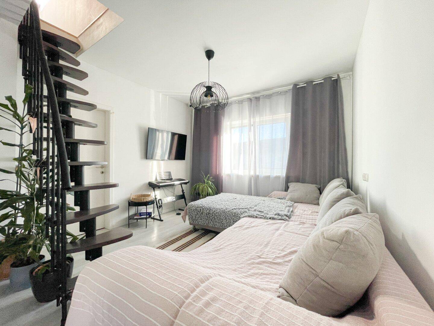 Gemütlicher Wohnbereich mit Sofa, Fernseher und einer eleganten offenen Treppe.
