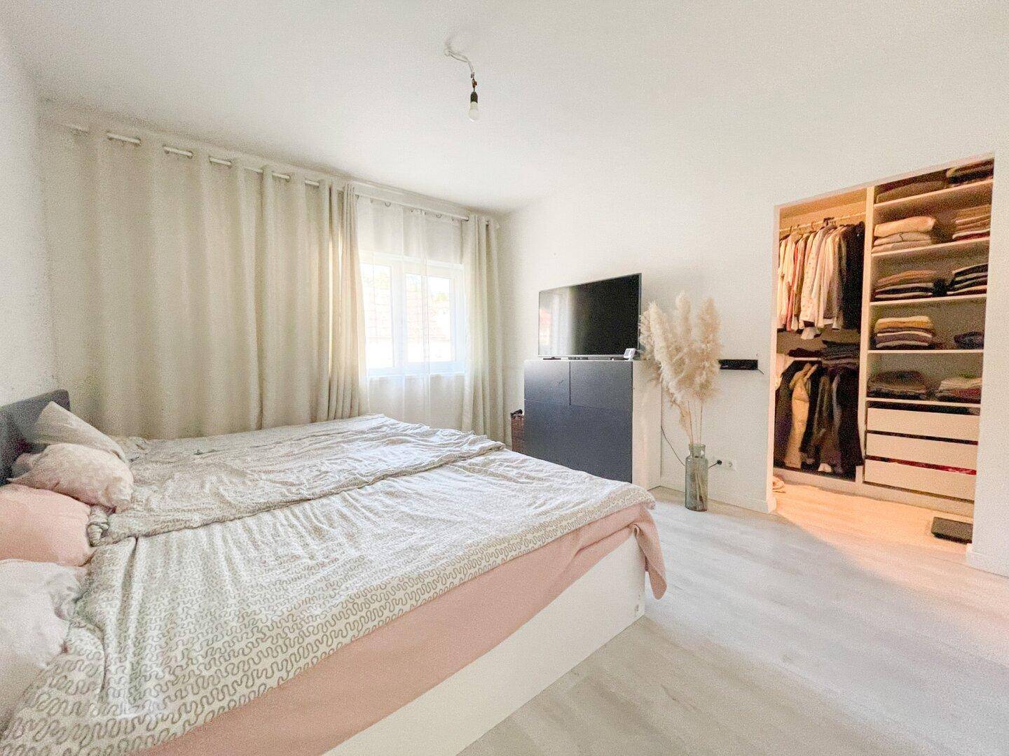 Helles Schlafzimmer mit Doppelbett, Fernseher und einem praktischen begehbaren Kleiderschrank.