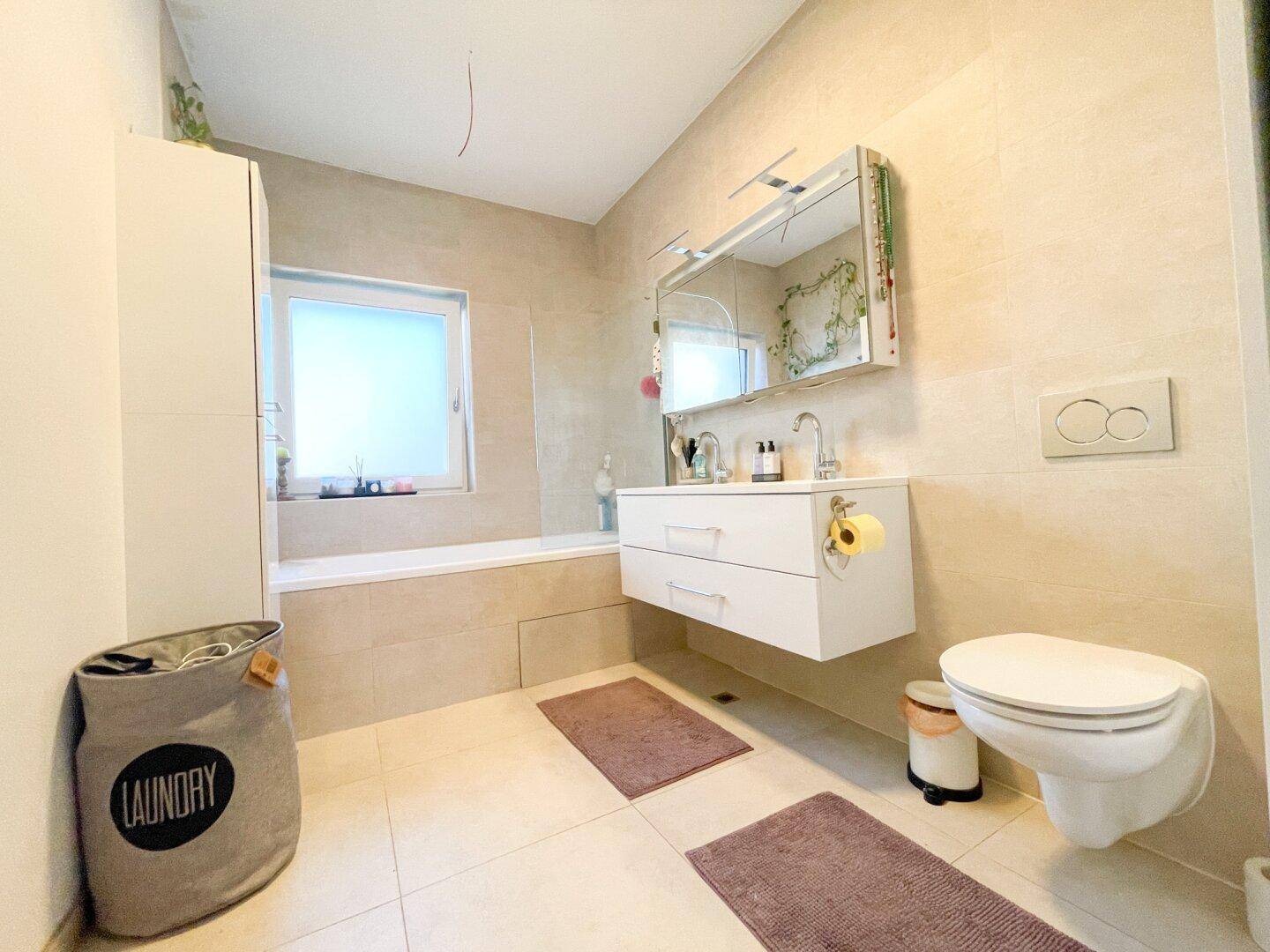 Modernes Badezimmer mit Badewanne, schwebendem Waschtisch, Toilette und Fenster.