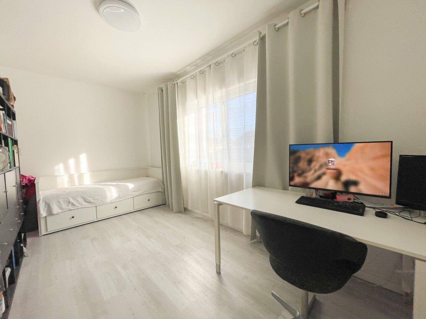 Funktionales Büro oder Gästezimmer mit Schreibtisch, Computer und viel Tageslicht.
