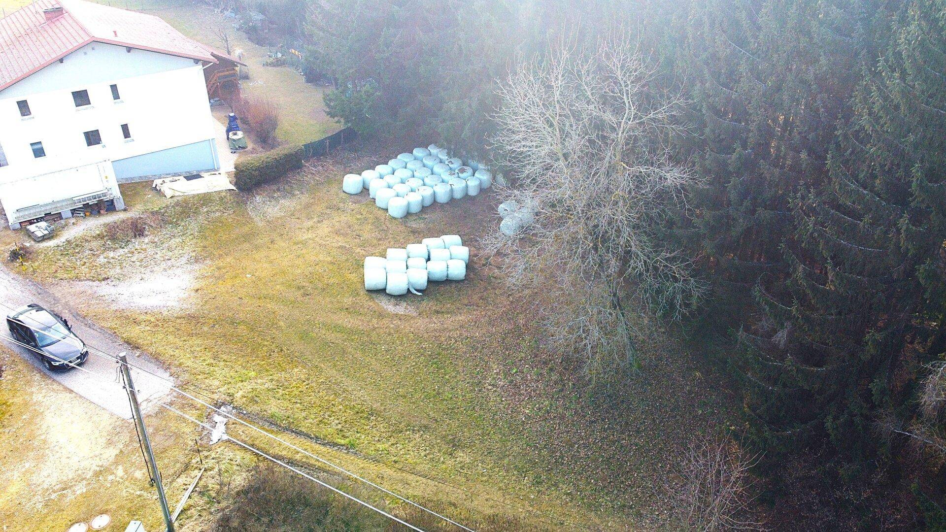Übersicht aus der Vogelperspektive auf ein Wohnhaus, angrenzenden Wald und landwirtschaftliche Ballen.