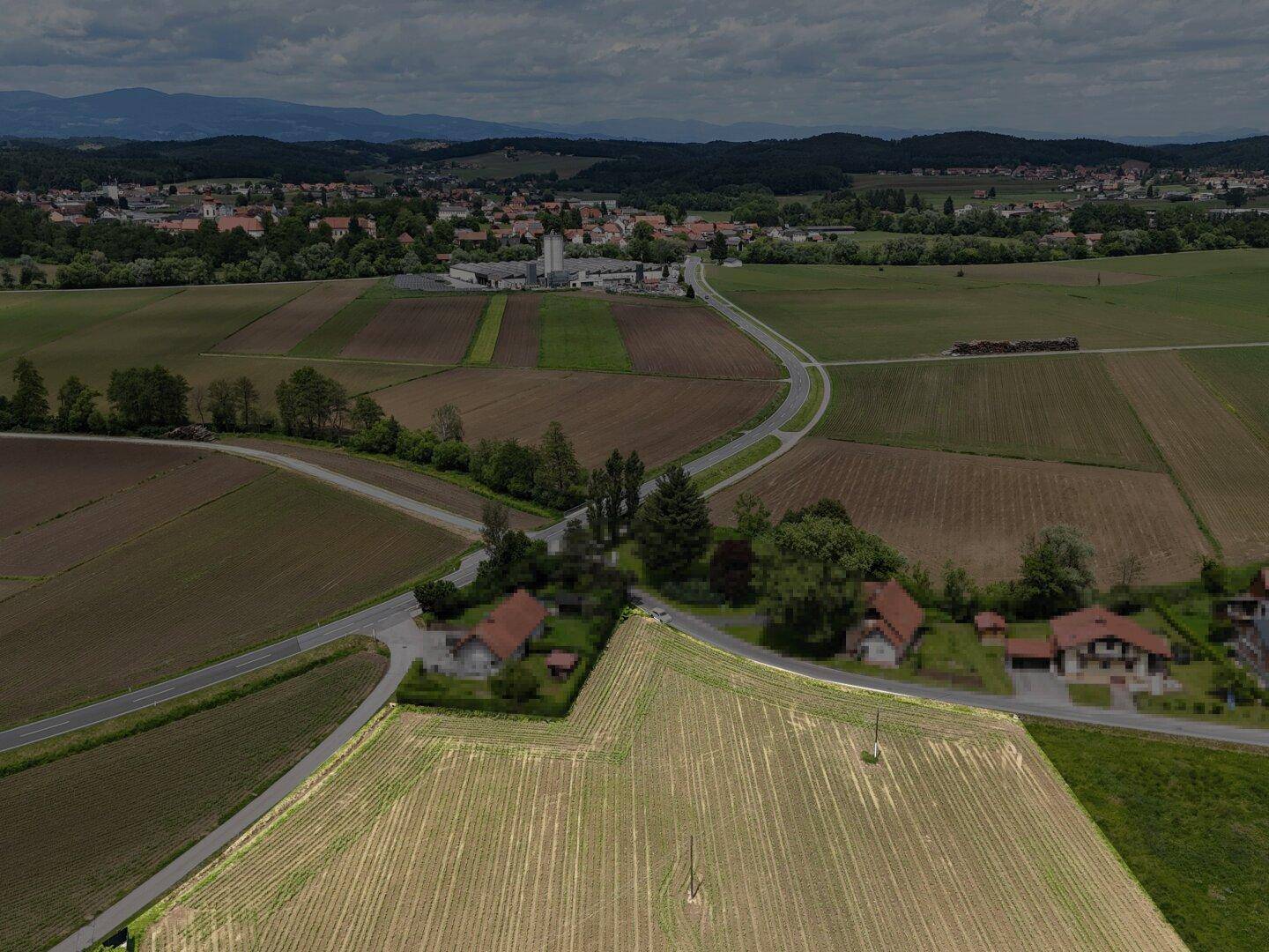 Weitläufige Luftaufnahme einer ländlichen Gegend mit Feldern, Straßen und einem Dorf in der Ferne.