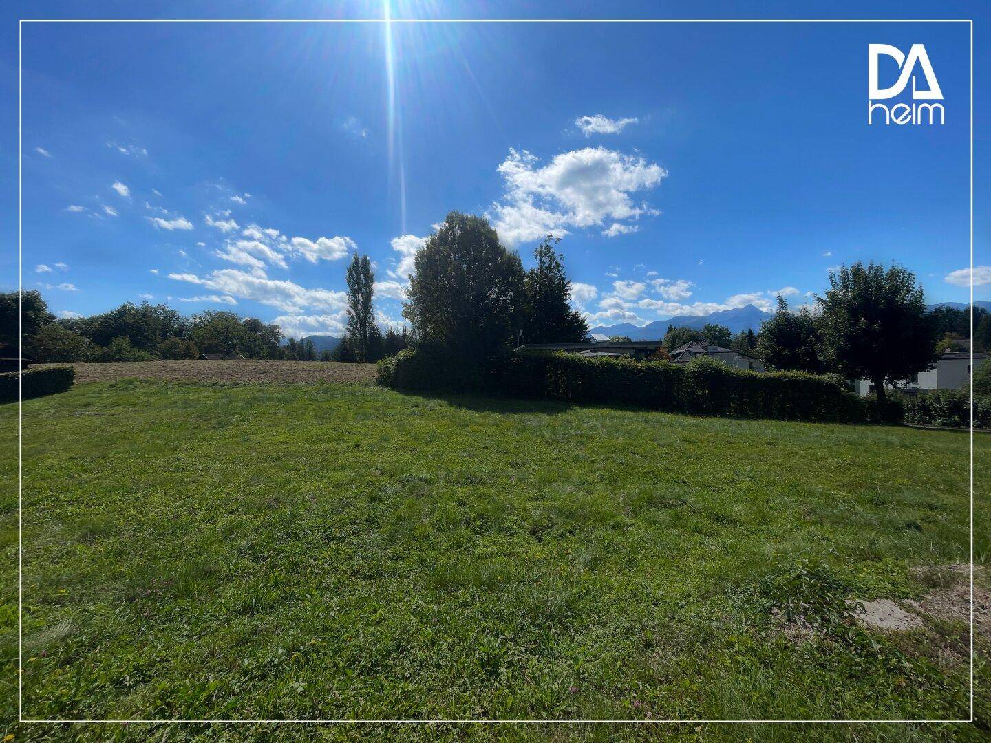 Sonniges, grünes Grundstück mit weitem Blick auf die umliegende Natur und Berge im Hintergrund.