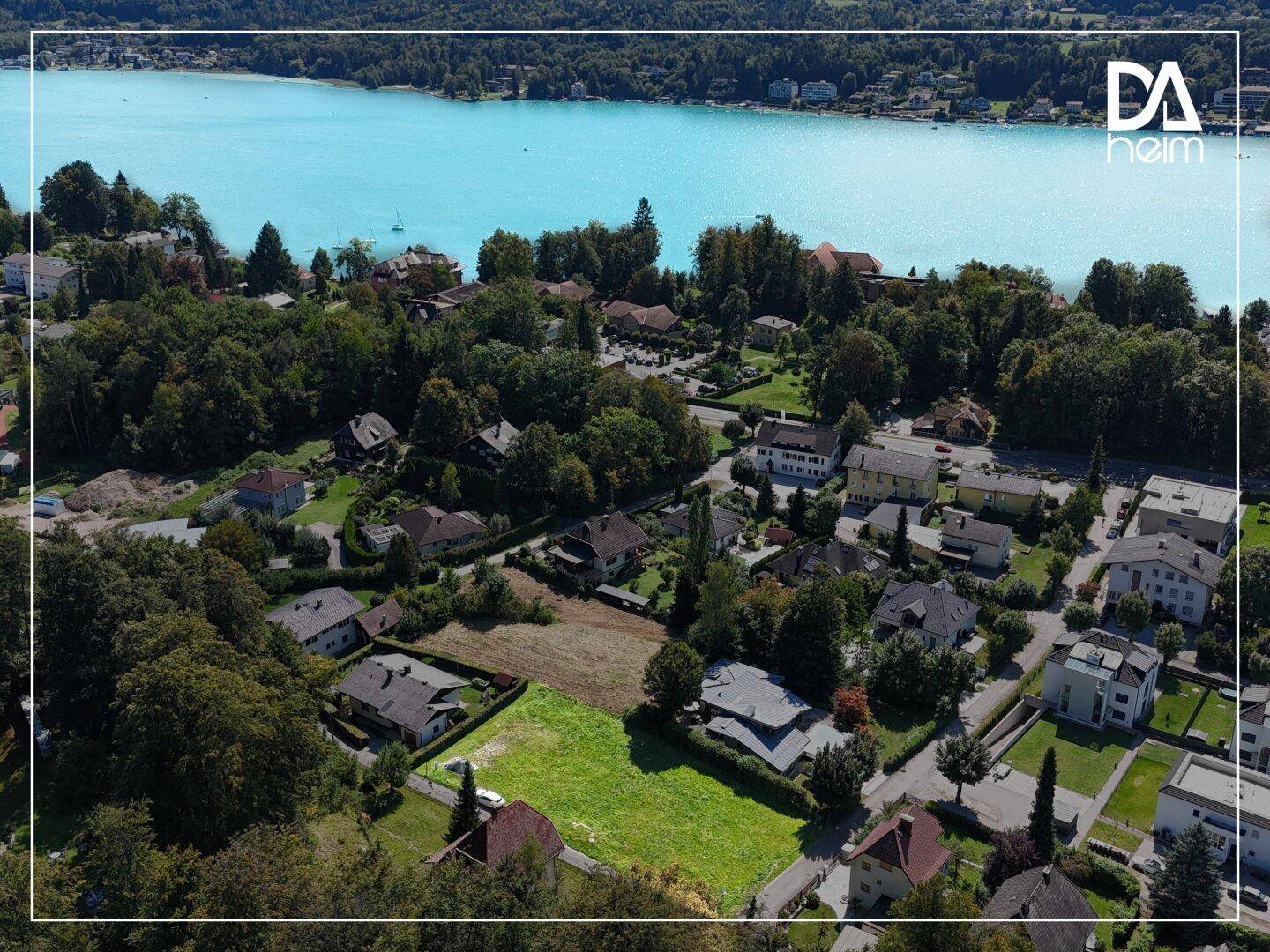 Weitläufige Luftaufnahme eines Wohngebiets mit See und Bergen im Hintergrund.