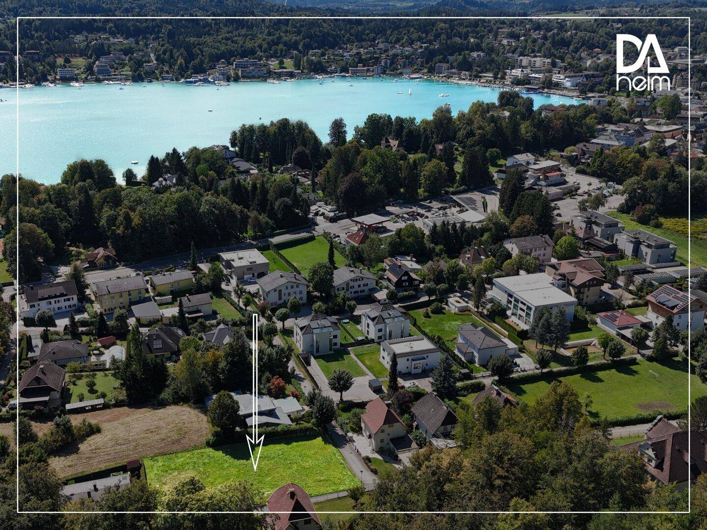 Luftaufnahme eines Grundstücks mit See im Hintergrund und umliegender Wohnbebauung.