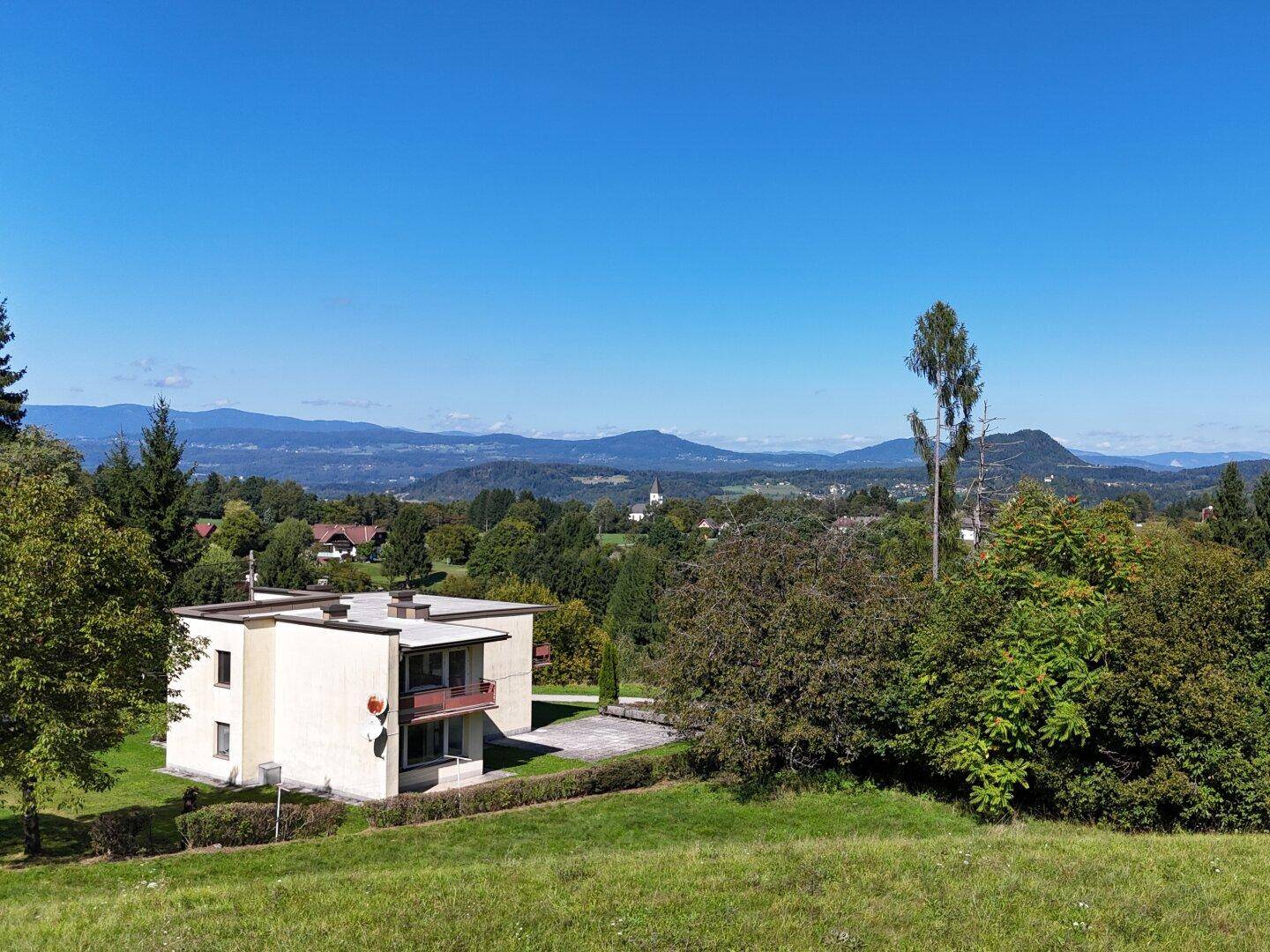 Panoramablick auf das Haus und die weite, grüne Landschaft mit Bergen im Hintergrund.