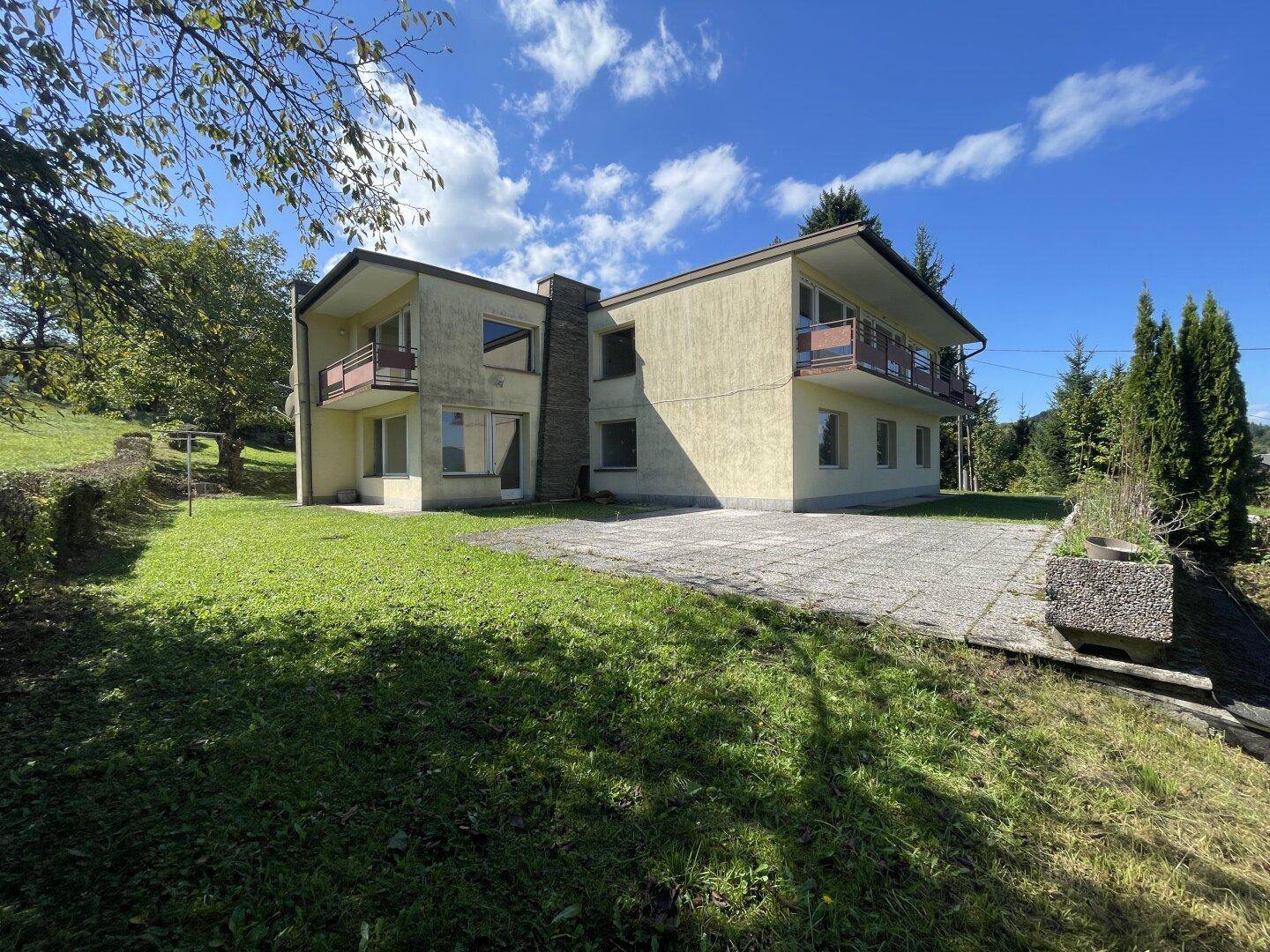 Ansicht des Hauses von der Seite mit großem Gartenbereich und gepflasterter Fläche.
