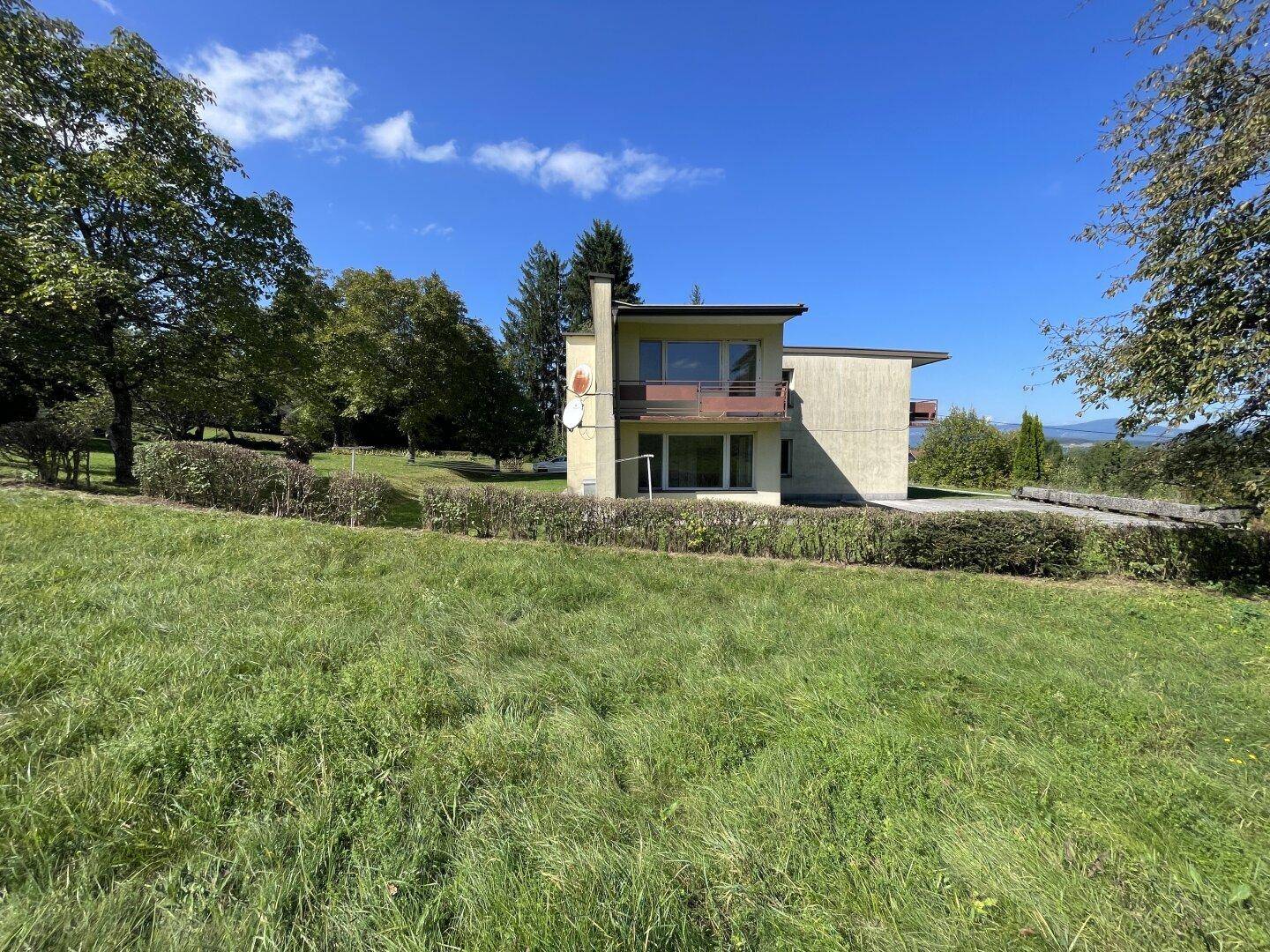 Ansicht des Hauses von einem großen, grünen Feld aus mit Bäumen im Hintergrund.