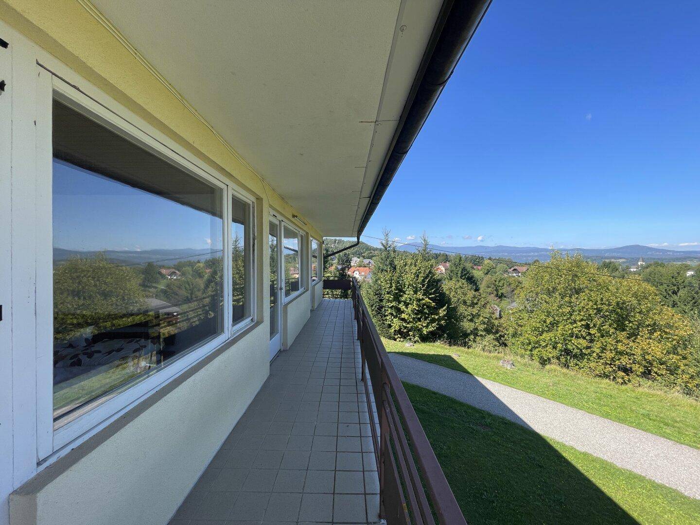 Langer Balkon mit Fliesenboden und weitem Blick über die grüne Hügellandschaft.