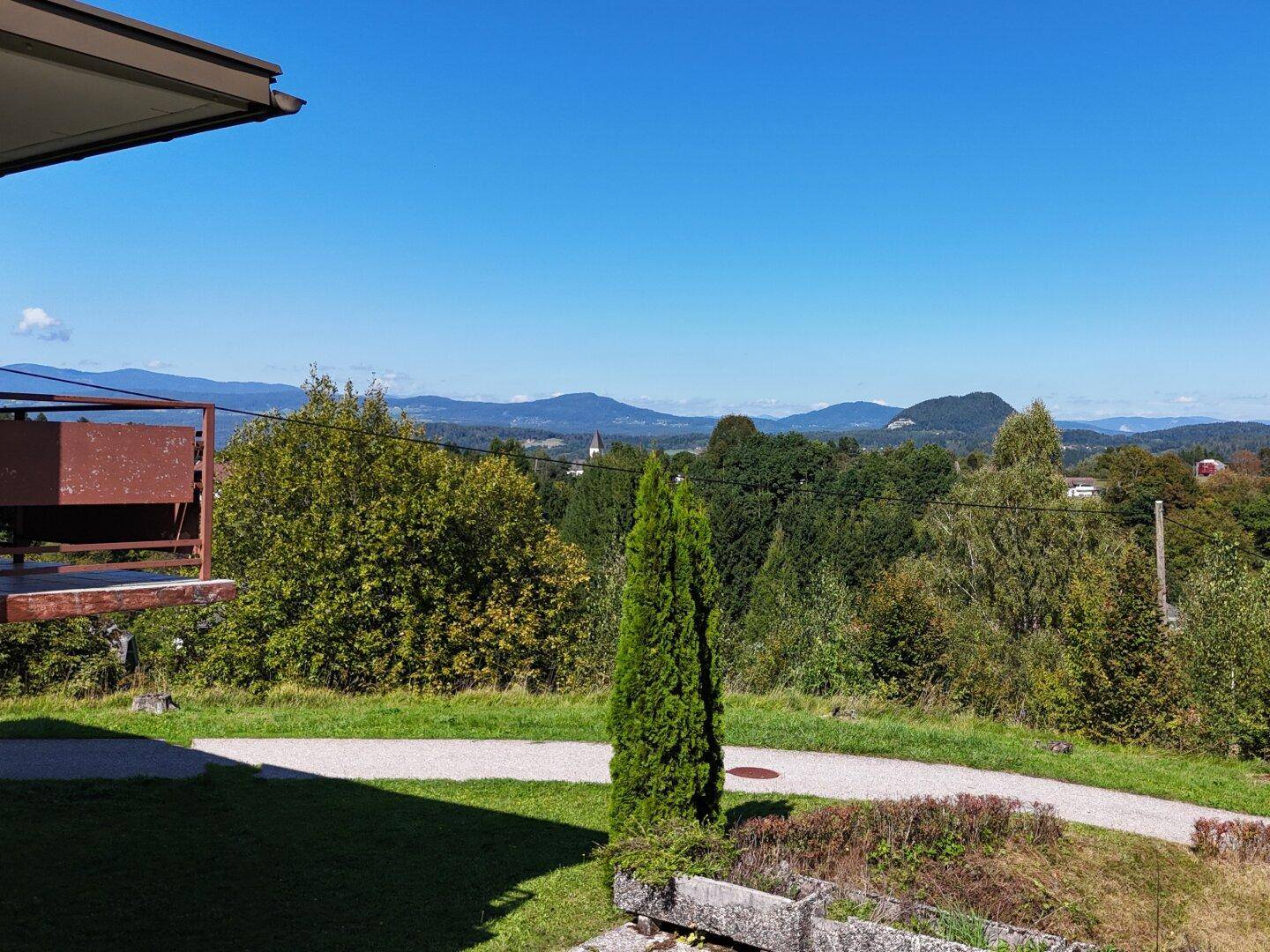 Weitläufige grüne Landschaft mit Bäumen und einem entfernten Dorf unter blauem Himmel.