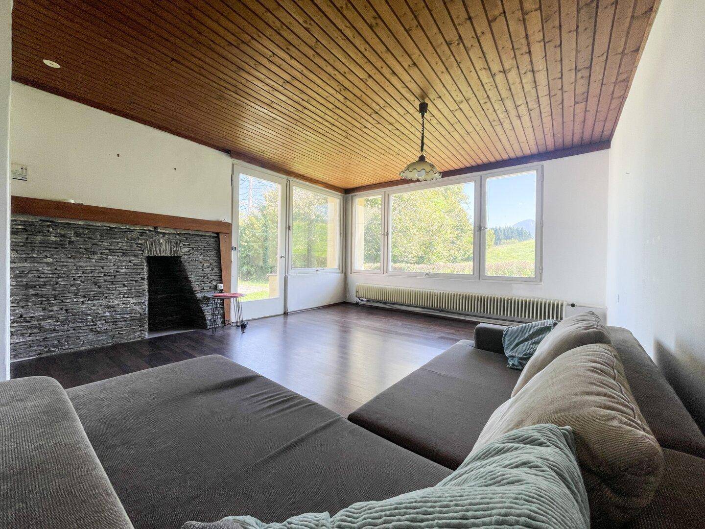 Geräumiges Wohnzimmer mit Holzbalkendecke, Kamin und großen Fenstern zur Natur.