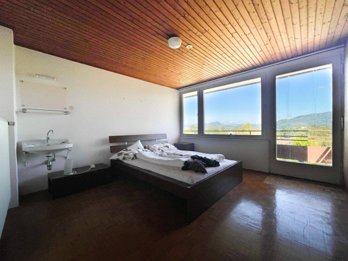 Helles Schlafzimmer mit Holzbalkendecke, Waschbecken und weitem Panoramablick.