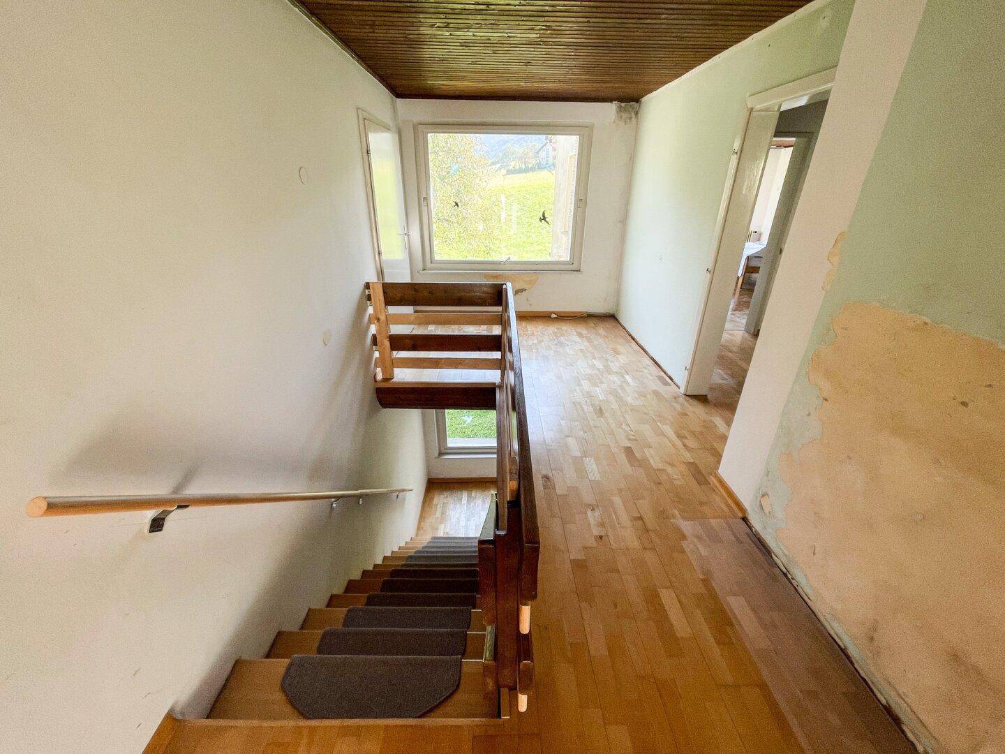 Treppenhaus mit Holzgeländer und Parkettboden, das zu den oberen Etagen führt.