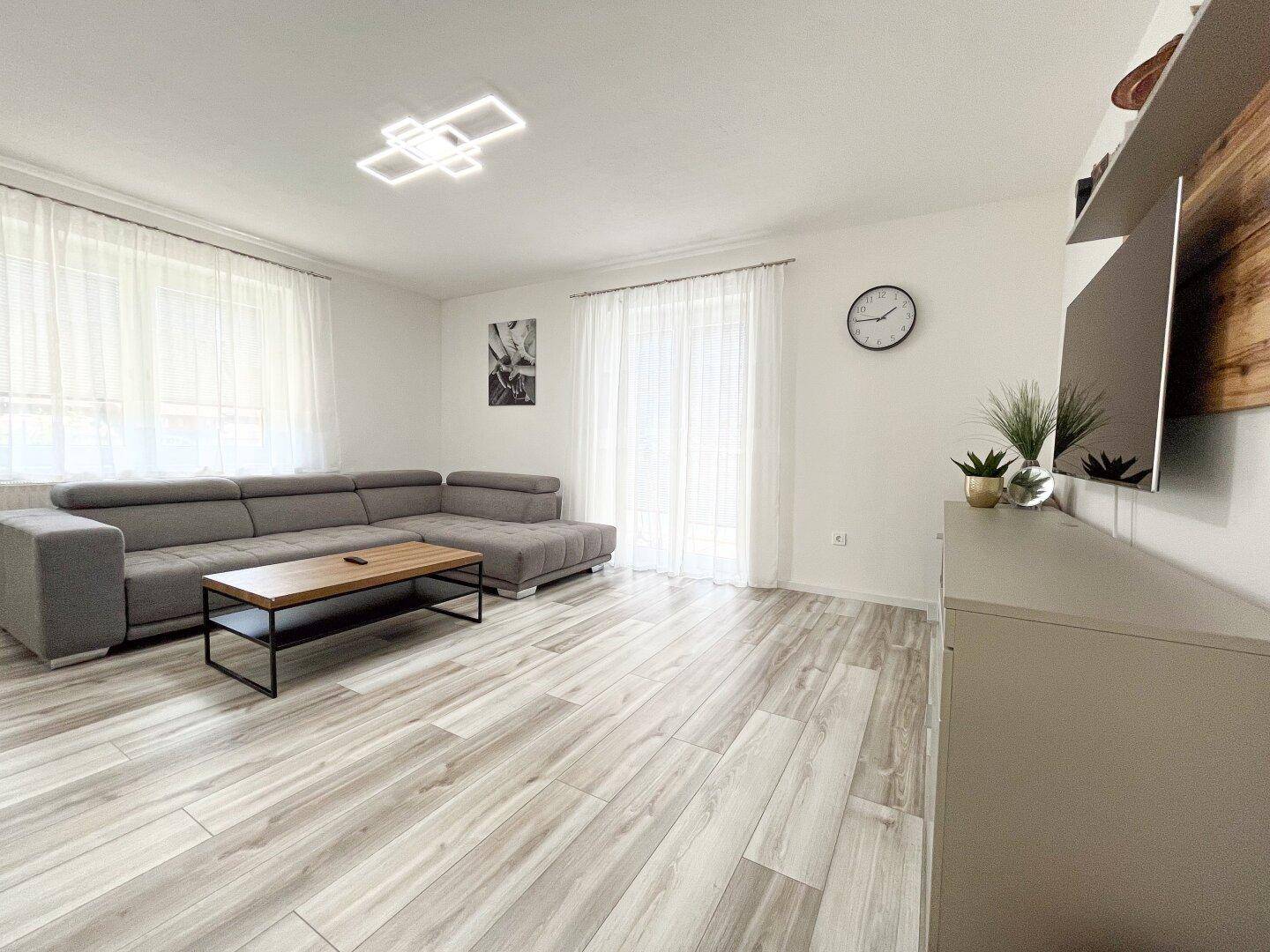 Helles Wohnzimmer mit modernem Sofa, Couchtisch und hellem Laminatboden.