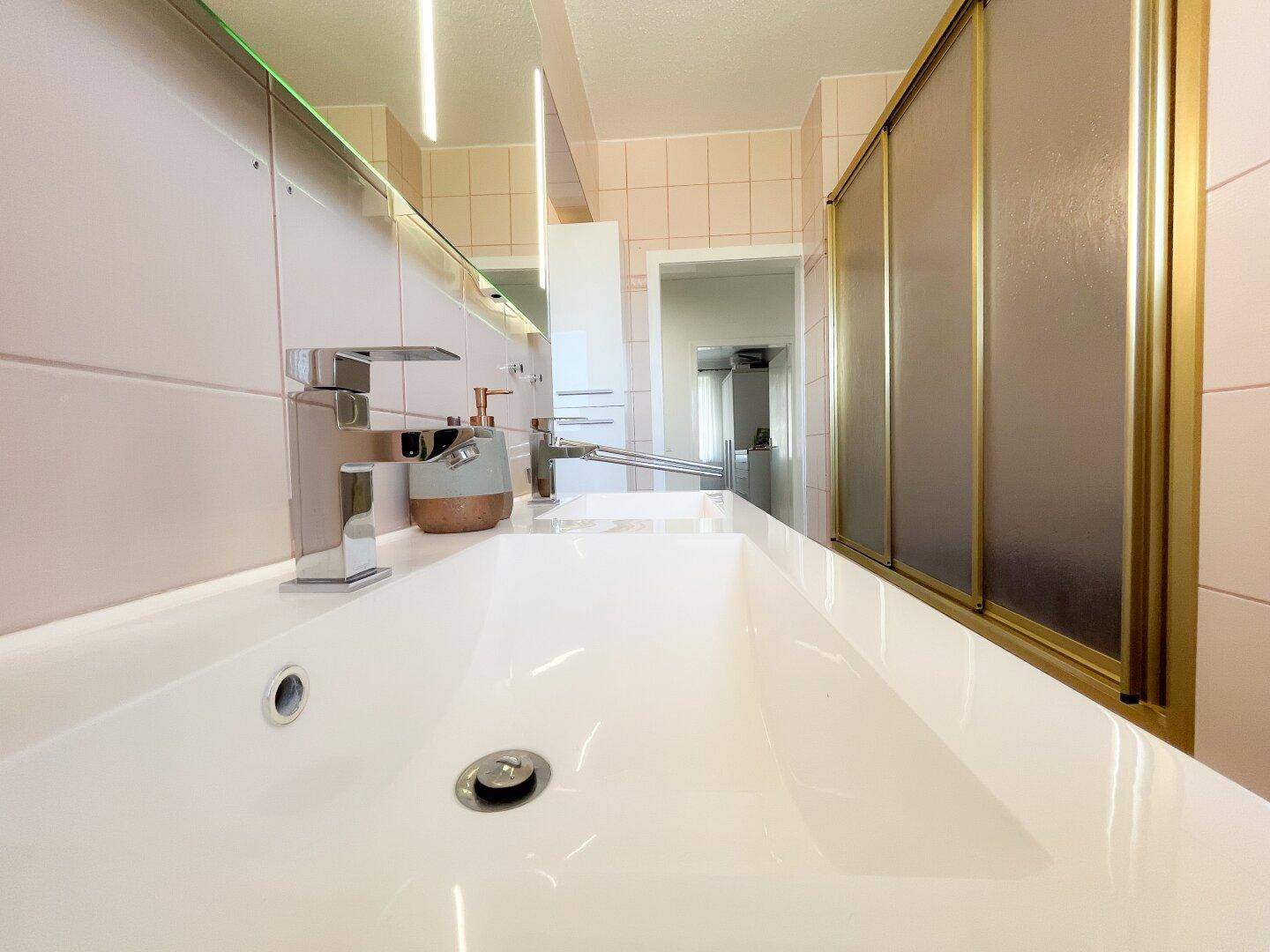 Badezimmer mit Einzelwaschbecken, Duschkabine und hellrosa Fliesen.