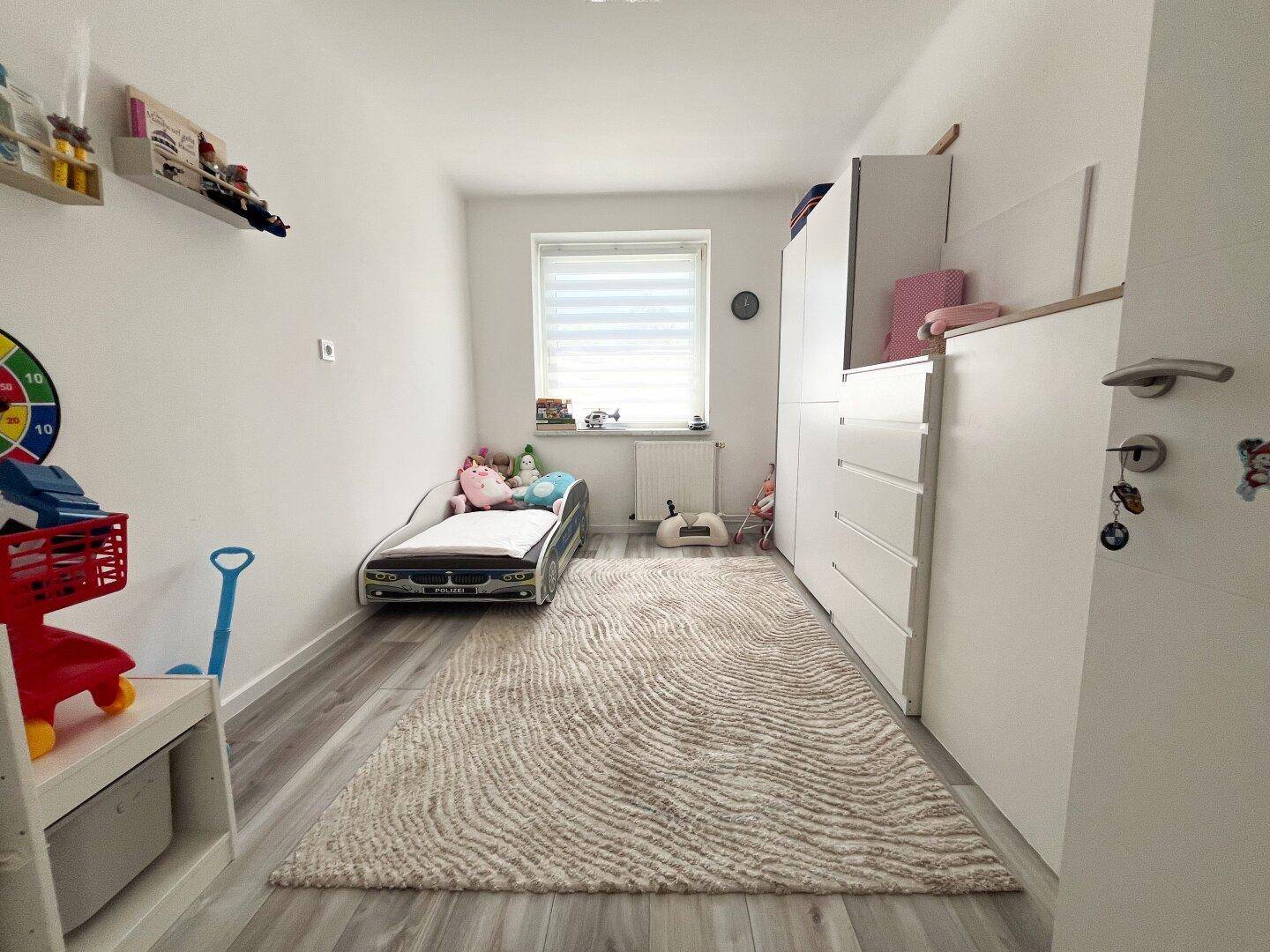 Kinderzimmer mit Einzelbett, weißem Kleiderschrank und hellem Teppichboden.