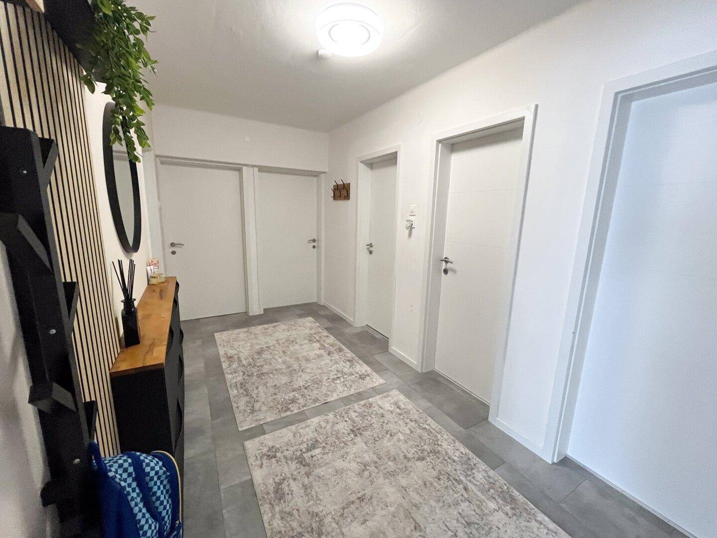 Heller Eingangsbereich mit Garderobe, Spiegel und modernem Bodenbelag.