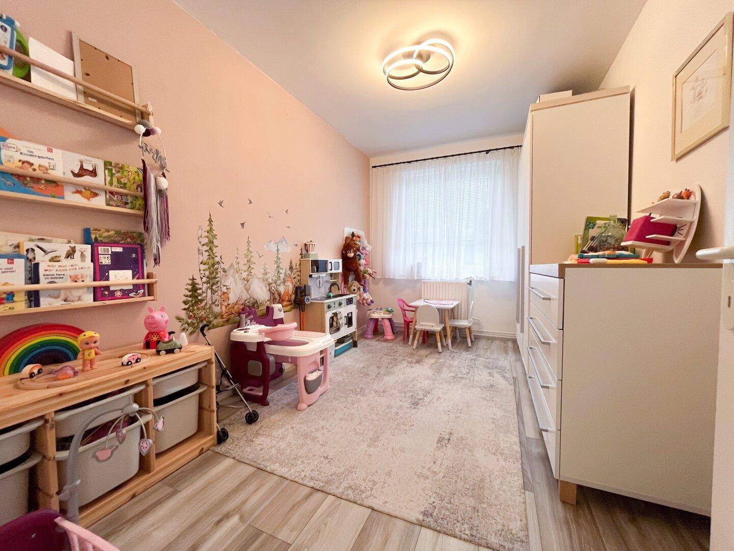 Kinderzimmer mit Spielbereich, rosa Wänden und hellem Teppichboden.