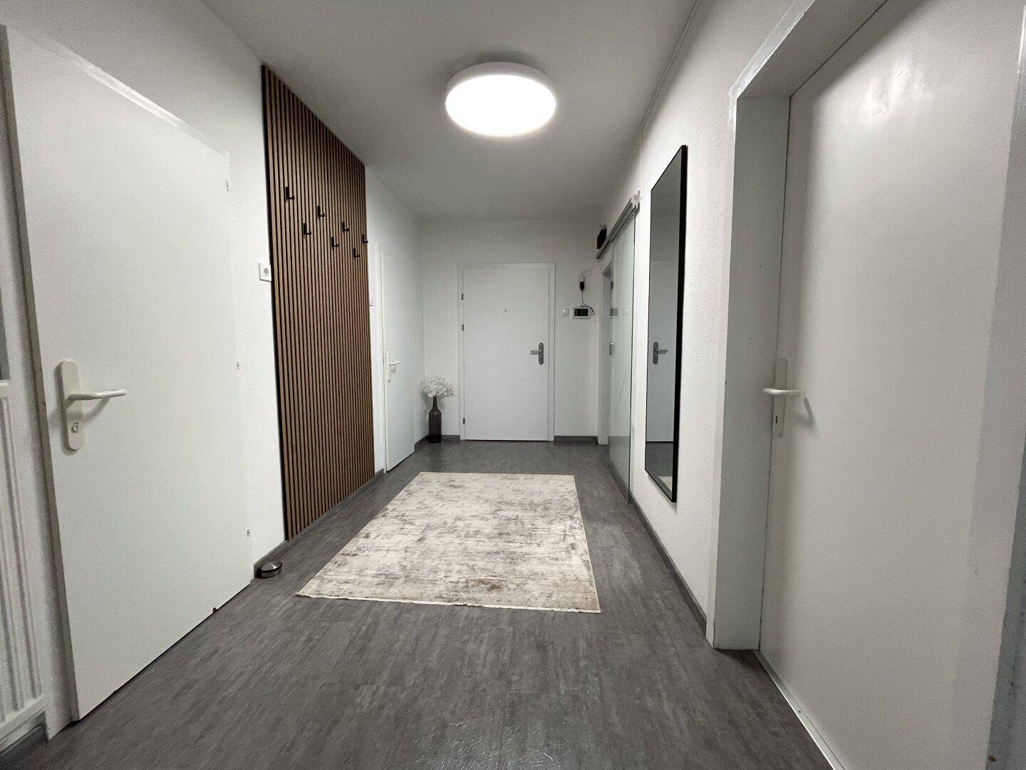 Heller Flur mit modernem Wandpaneel, Spiegel und dunklem Bodenbelag.