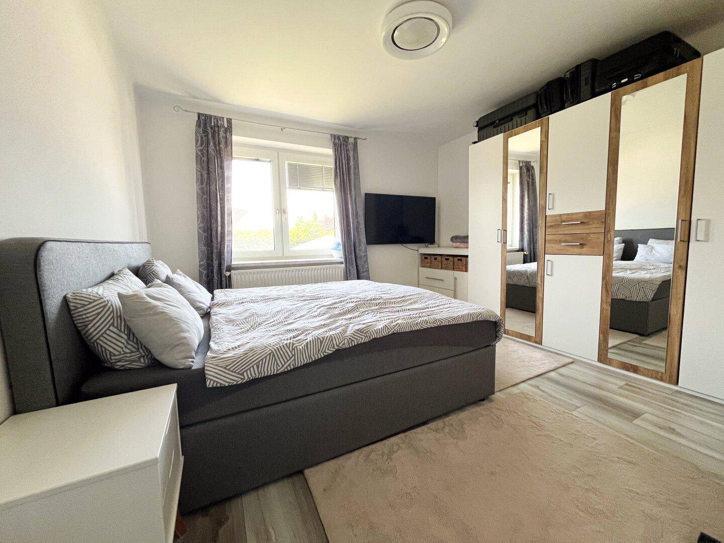 Schlafzimmer mit Doppelbett, Spiegelschrank und hellem Laminatboden.