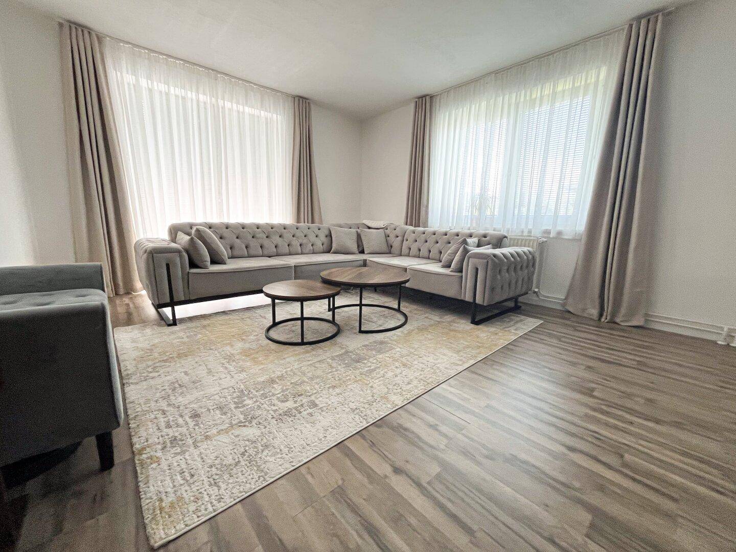 Geräumiges Wohnzimmer mit großem Ecksofa, Couchtischen und hellem Laminatboden.