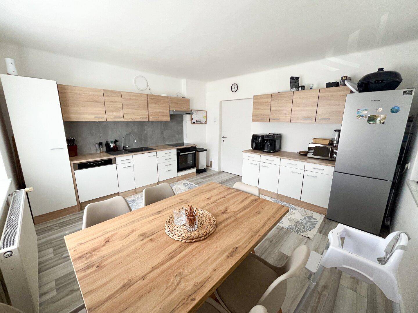 Helle Einbauküche mit Essbereich, modernen Geräten und Holzakzenten.