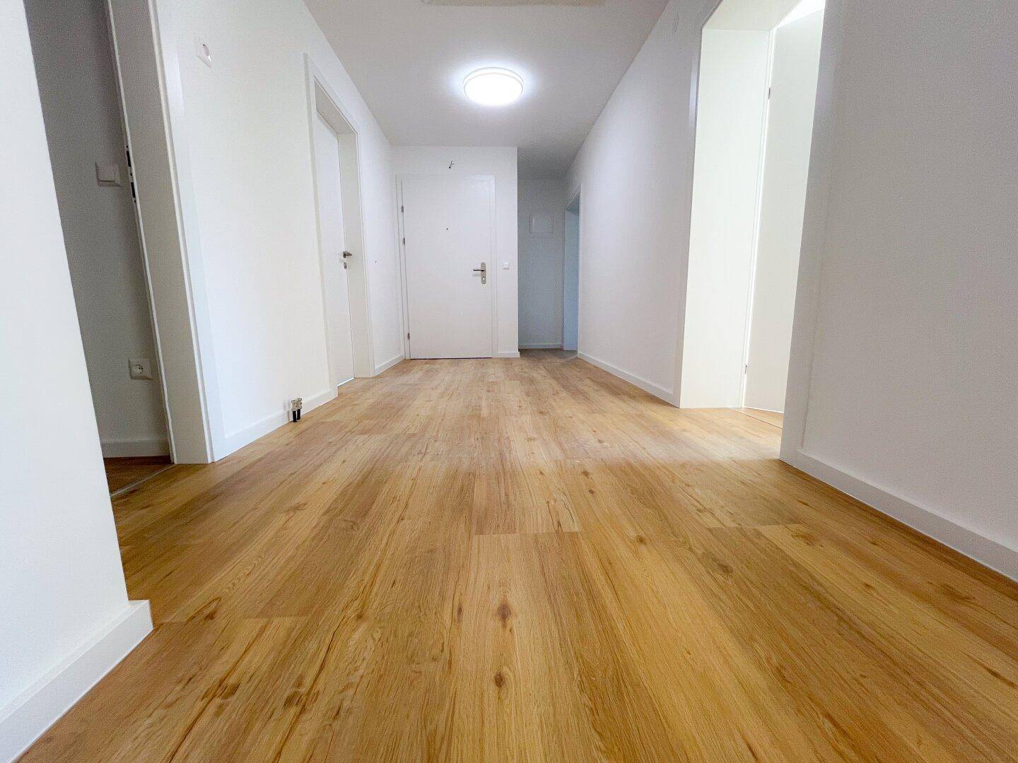 Heller Flur mit Holzoptik-Laminatboden und weißen Wänden.