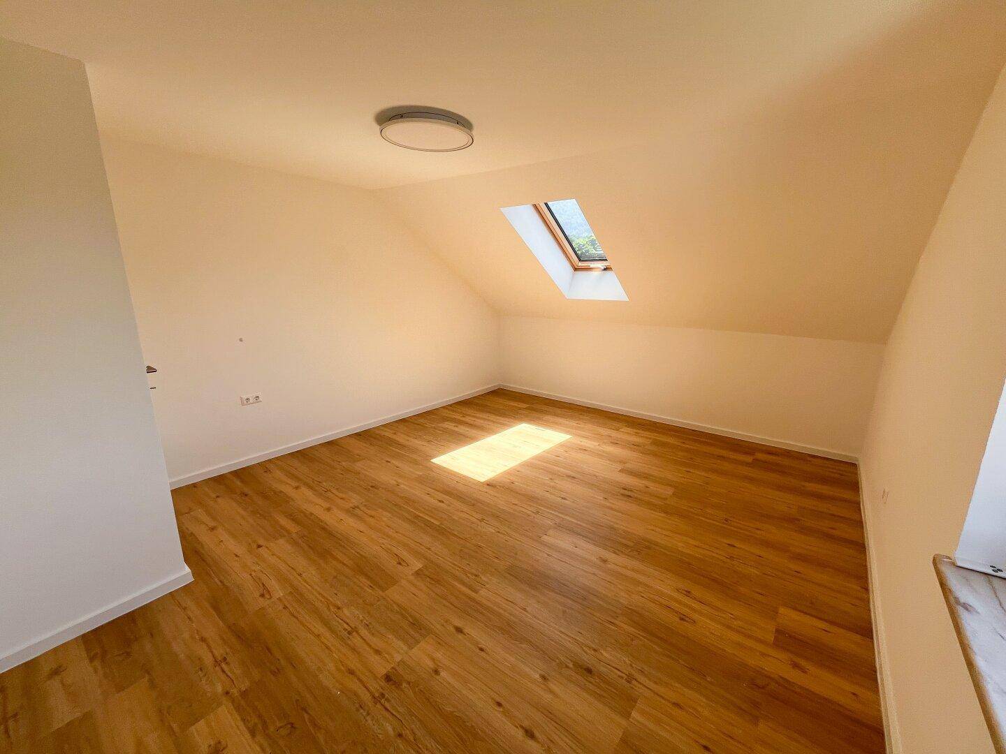 Helles Schlafzimmer im Dachgeschoss mit Dachfenster und Laminatboden.