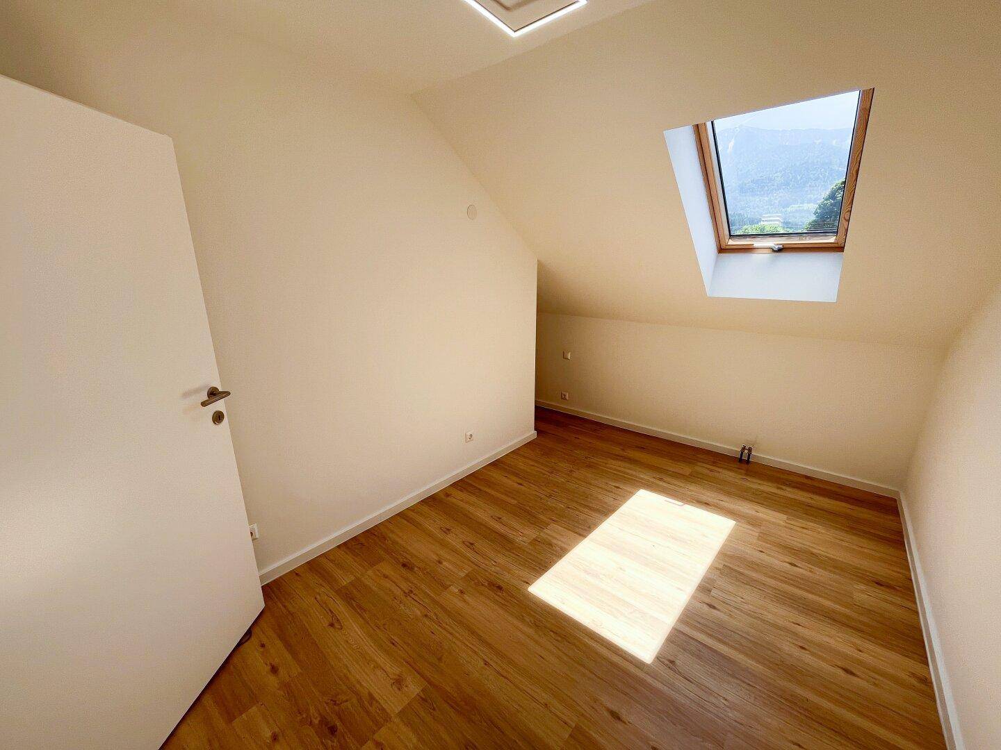 Helles Schlafzimmer im Dachgeschoss mit Dachfenster und Laminatboden.