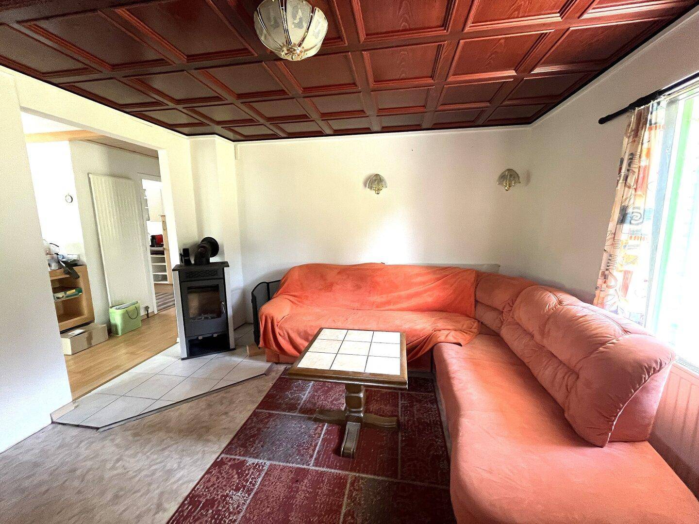 Gemütliches Wohnzimmer mit Holzkassettendecke, Kaminofen und bequemer Eckcouch.