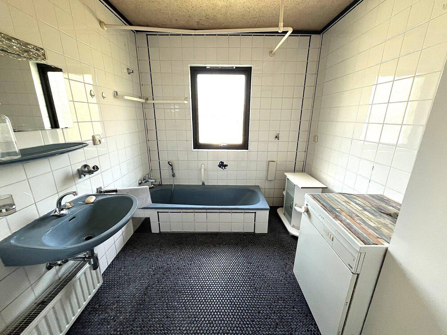 Badezimmer im Stil der 80er Jahre mit blauer Badewanne, weißen Fliesen und Fenster.