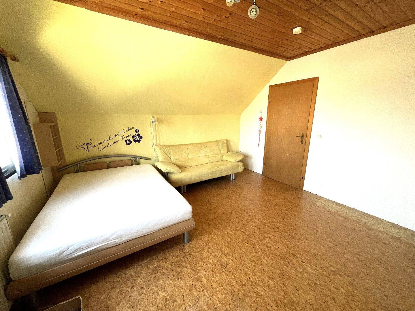 Schlafzimmer im Dachgeschoss mit Dachschräge, Holzbalkendecke und hellem Bodenbelag.