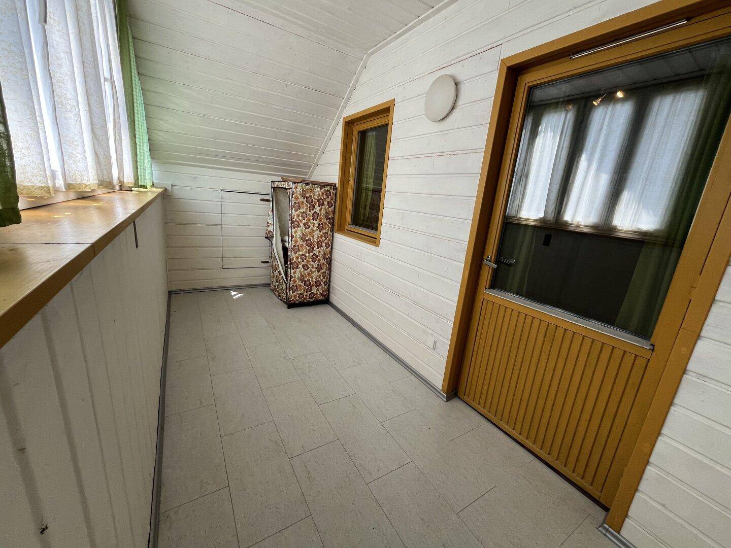 Überdachter Balkon mit Holzverkleidung, Fliesenboden und Blick ins Grüne.