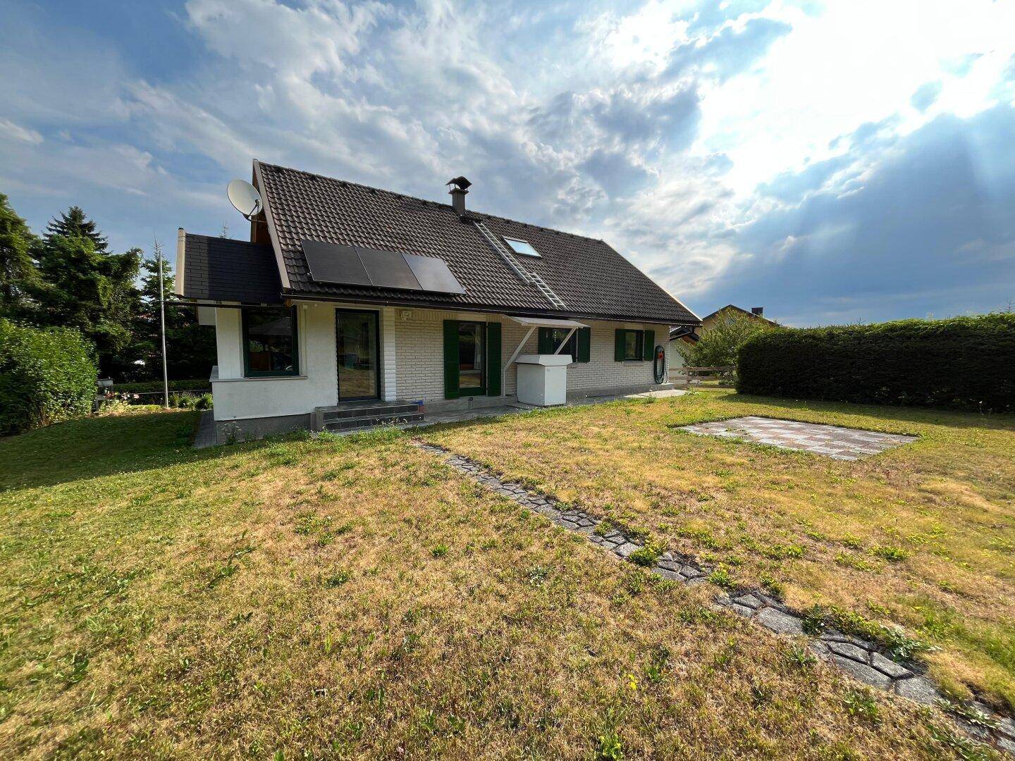 Hausansicht mit großem Garten, Photovoltaikanlage und sonnigem Außenbereich.