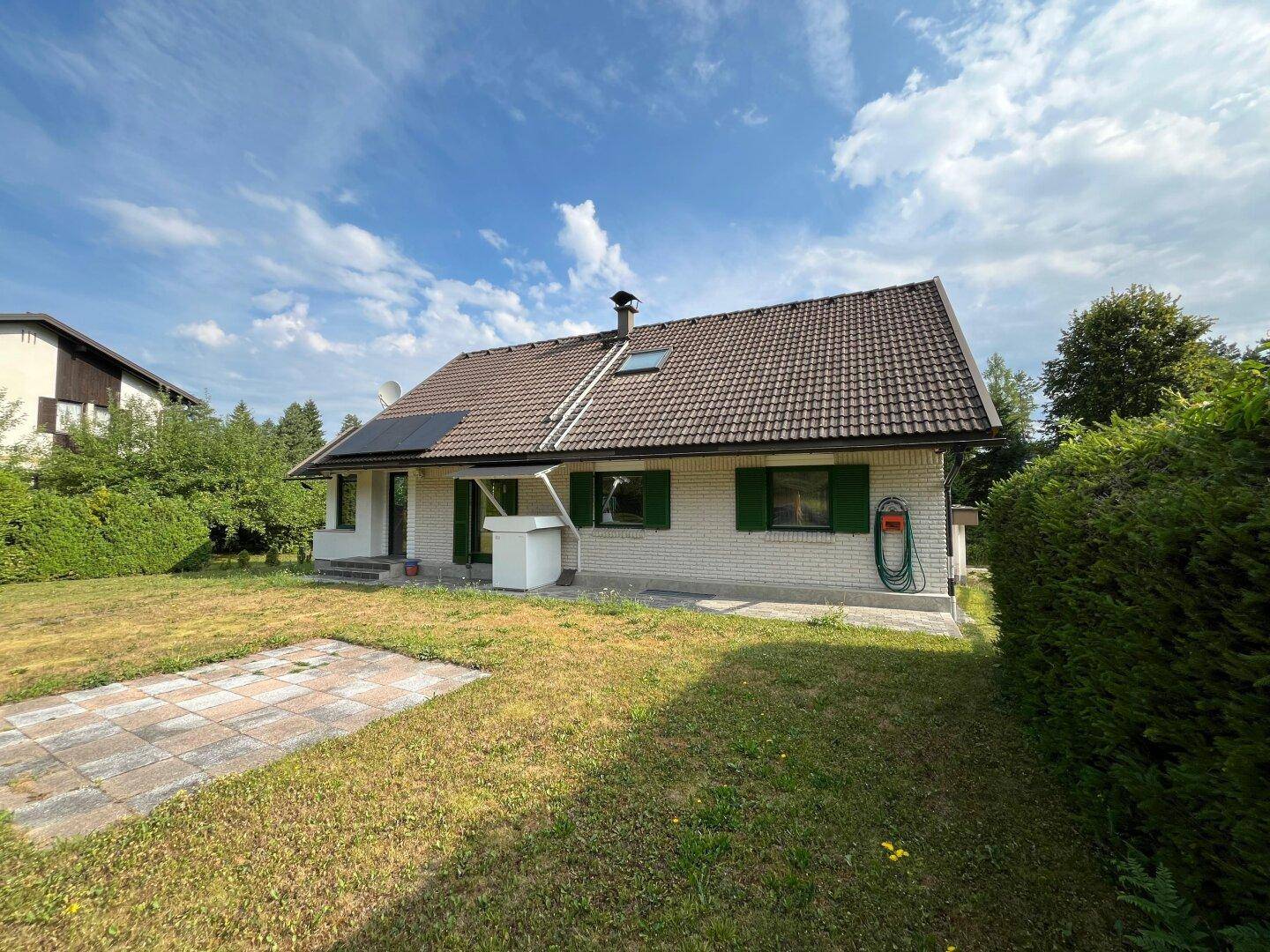 Seitenansicht des Hauses mit Garten, Hecke und sonnigem Außenbereich.
