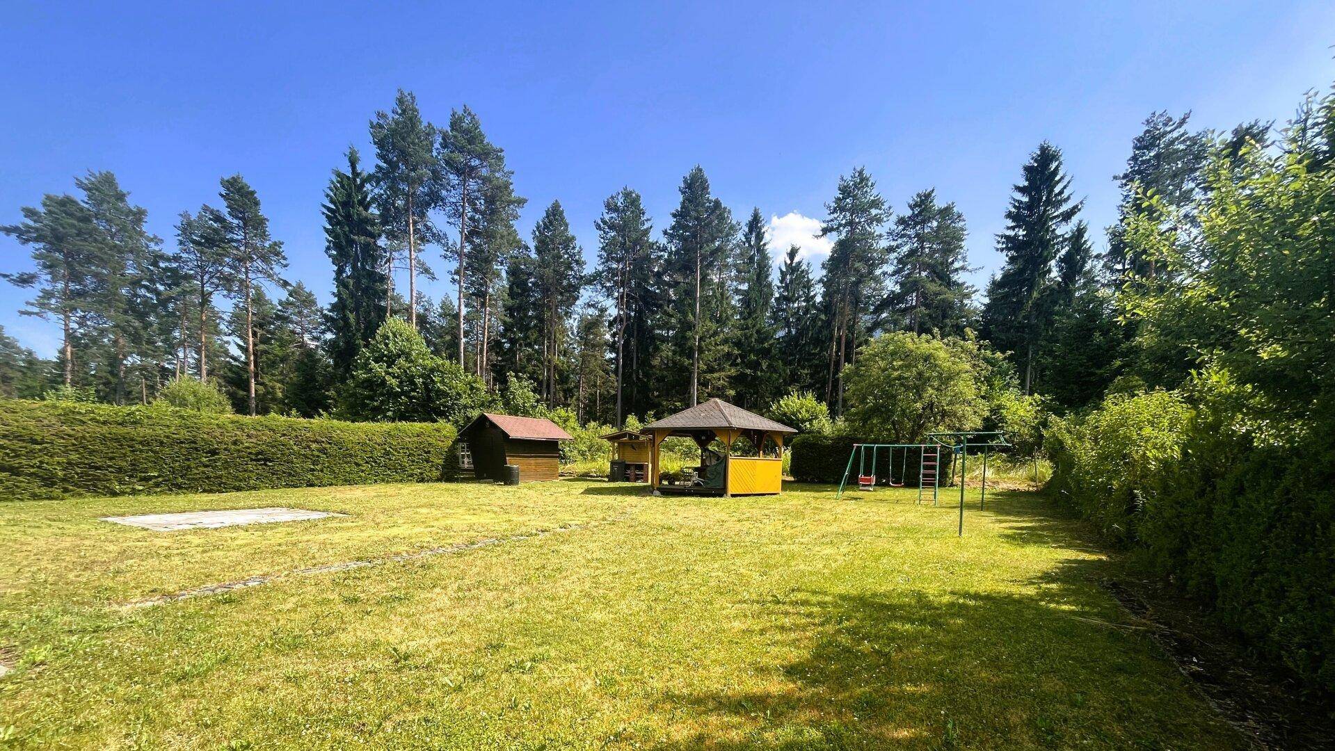 Weitläufiger Gartenbereich mit Rasen, Spielplatz, Gartenhaus und umgebenden Bäumen.