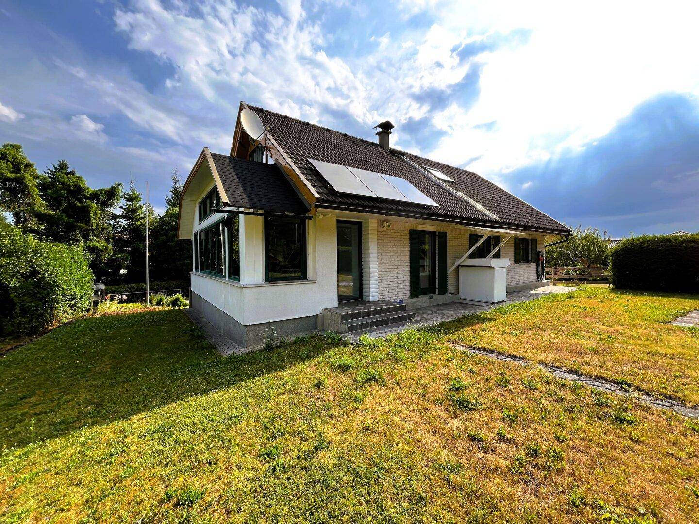 Hausansicht mit Photovoltaikanlage auf dem Dach, weißer Fassade und grünem Garten.