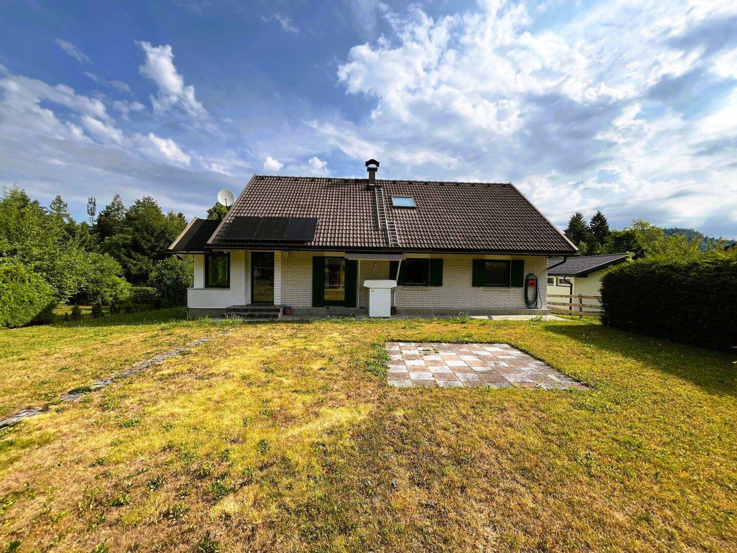 Rückansicht des Hauses mit großer Rasenfläche, kleiner Terrasse und Photovoltaikanlage.