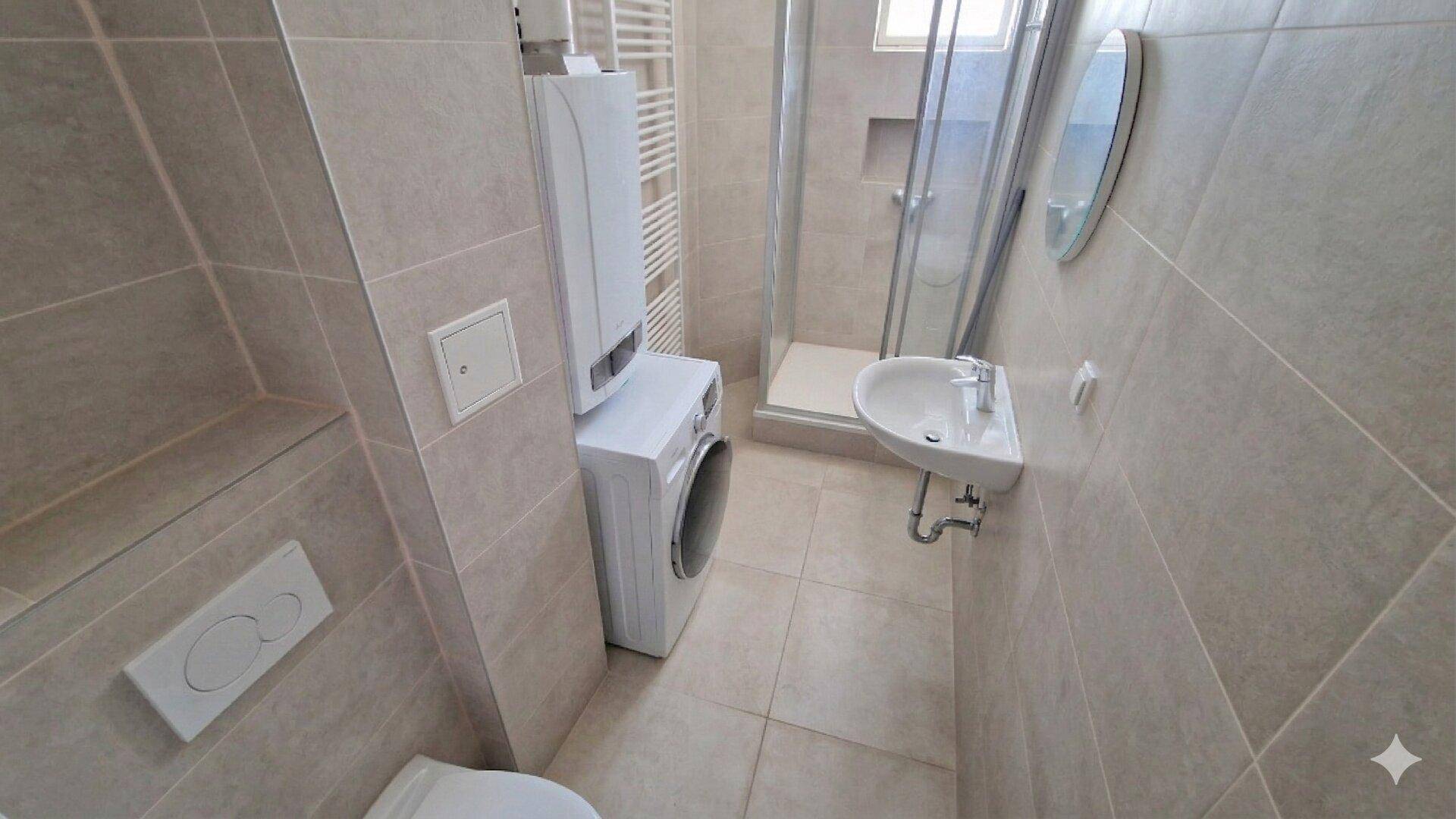 Modernes Badezimmer mit beigefarbenen Fliesen, Dusche, Waschmaschine und Handtuchheizkörper.