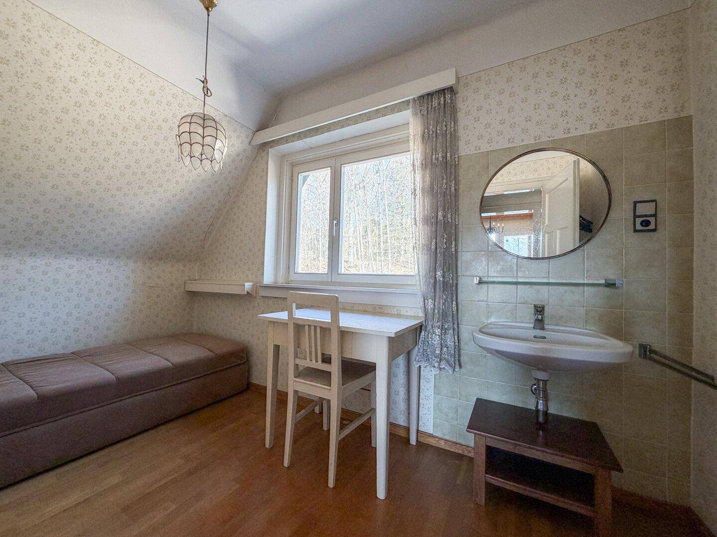 Helles Zimmer mit Einzelbett, Schreibtisch und integriertem Waschbecken, ideal als Gästezimmer.