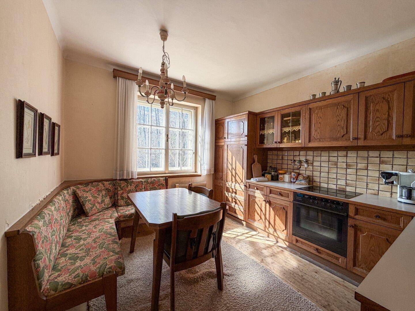 Traditionelle Wohnküche mit Holzeinbauten, Essecke und Fenster mit Blick ins Grüne.