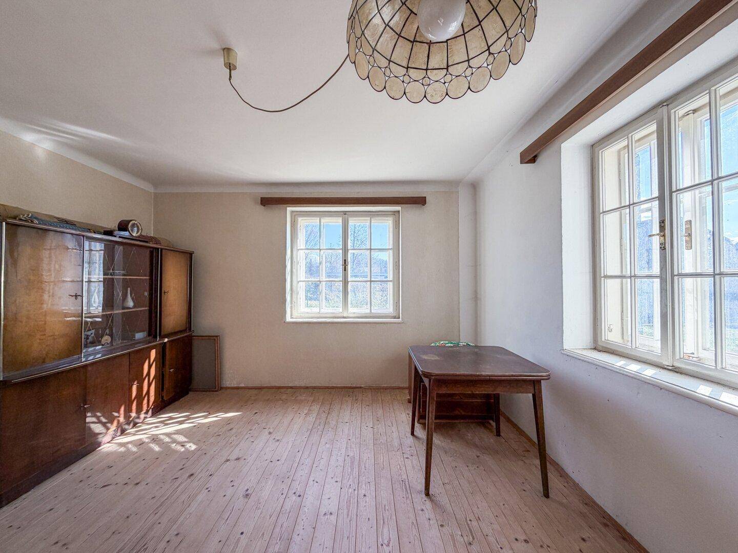 Helles Zimmer mit Holzboden, großem Fenster und einem antiken Schrank, viel Tageslicht.