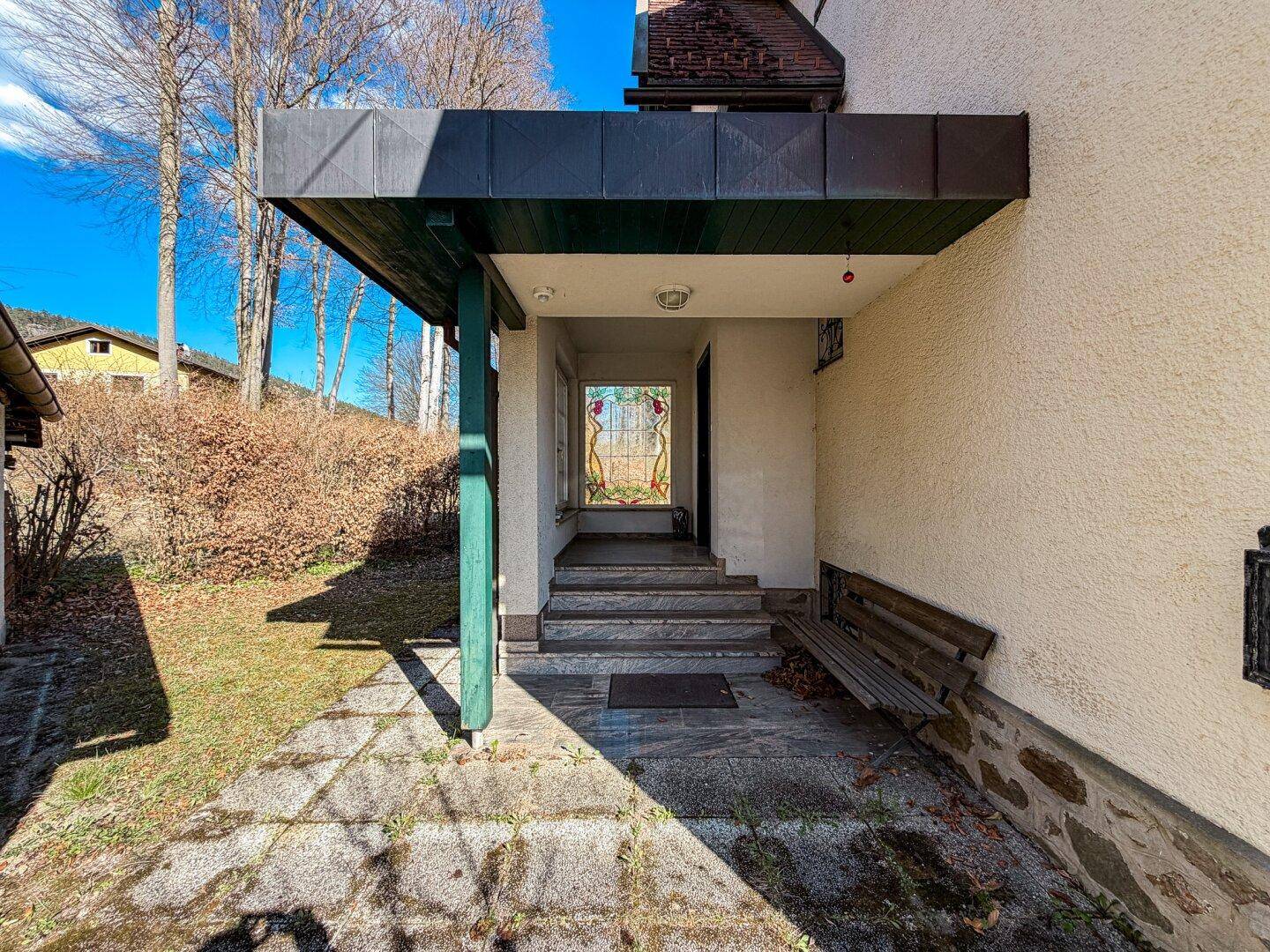 Überdachter Eingangsbereich des Hauses mit Steinstufen und einer Holzbank, einladend gestaltet.